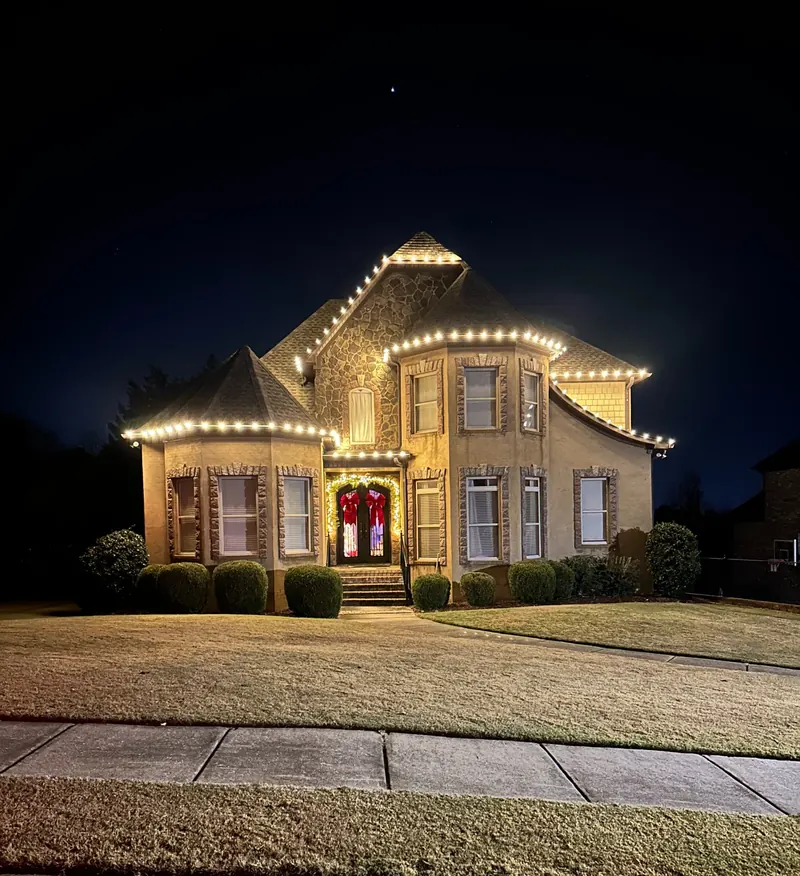 Warm roofline Christmas lights on a large stone-front home at night in the Trussville area